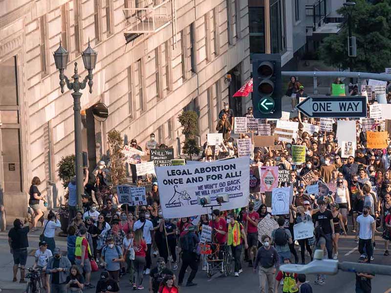 a bird's eye view of a large group of people holding up signs and parading down a street in protest
